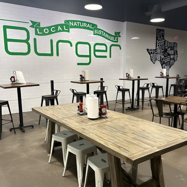 BuffBurger restaurant interior with wooden tables, black high-top tables, and a large green "Burger" sign.