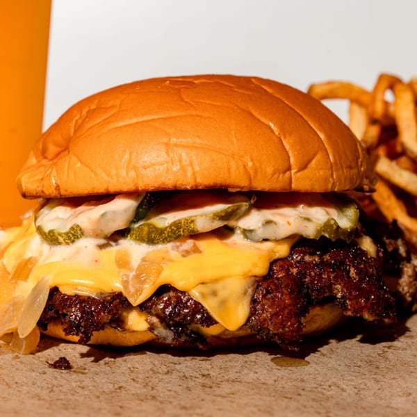 Close-up of a BuffBurger with melted cheese, pickles, and sauce, with fries in the background.