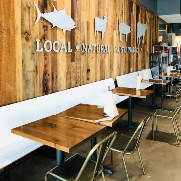 BuffBurger's dining area with wooden tables, white benches, and a wooden wall with "LOCAL NATURAL SUSTAINABLE" text.