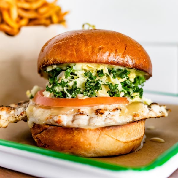 A BuffBurger chicken sandwich with melted cheese, tomato, and kale slaw on a brioche bun.