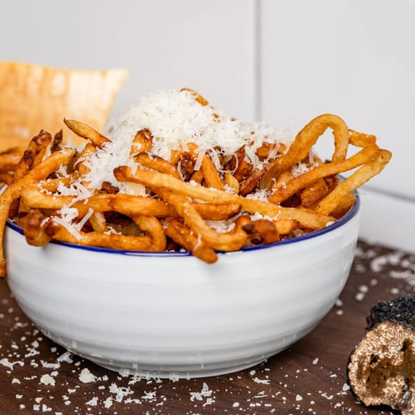 A white bowl filled with golden-brown BuffBurger fries, generously topped with grated Parmesan cheese.