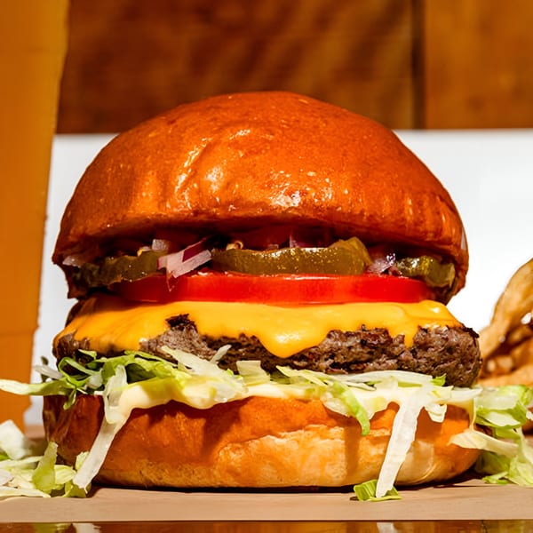 A BuffBurger cheeseburger with lettuce, tomato, pickles, and onions on a brioche bun.